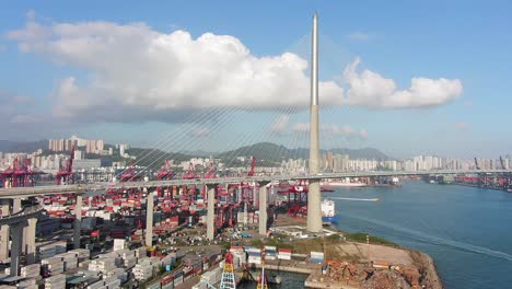 Traffic-on-Stonecutters-bridge,-Hong-Kong-with-Container-terminal-and-port-at-Victoria-bay,-storage-terminal-and-docked-Ships,-Aerial-view-on-a-beautiful-clear-day