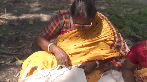 Rural-old-Indian-tribal-woman-sewing-or-stitching-cloths-outdoor,-feminism-and-self-independent-woman