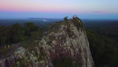 Aerial-shot-of-mount-Tinbeerwah-lookout-at-sunset-with-people,-forests-and-pink-clouds