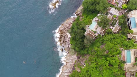 Phuket,-Thailand,-Top-down-aerial-view-of-cliffside-resorts,-surrounded-by-lush-green-nature-and-Sea