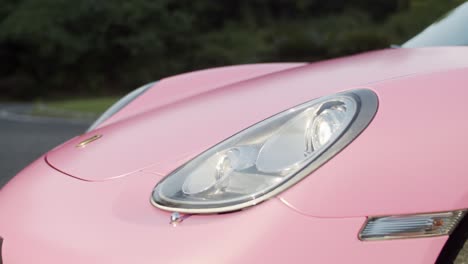 Front-headlight-of-pink-coated-Porsche-Boxster-two-seater-sports-car