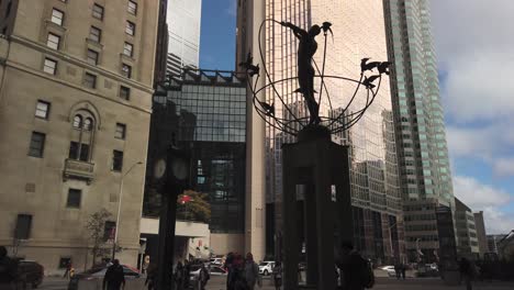Wide-view-of-people-on-the-sidewalk-at-Union-Station-in-Toronto,-with-slow-tilt-up-to-Royal-Bank-tower-and-view-of-statue
