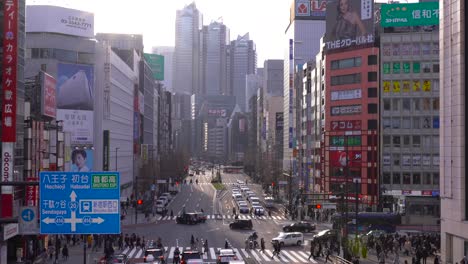 Menschen-überqueren-Die-Fußgängerzone-In-Der-Belebten-Straße-Von-Shinjuku,-Tokio,-Japan,-Mit-Fahrzeugen-Bei-Wenig-Verkehr-–-Nach-Unten-Geneigter-Schwenk