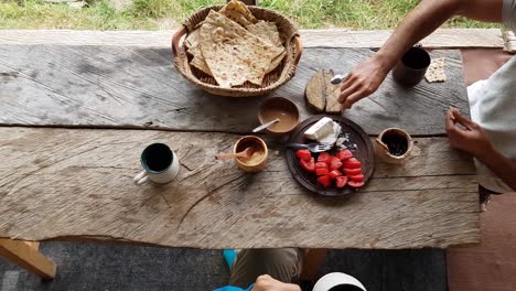 Soziale-Kommunikation-Am-Esstisch-Beim-Morgendlichen-Frühstück-Mit-Holztisch,-Korb,-Fladenbrot,-Marmelade,-Tomate,-Käse,-Tee,-Kaffeegetränk