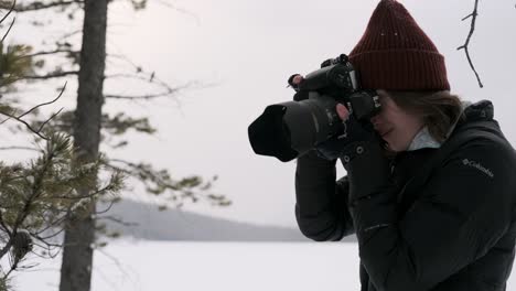 A-Young-Female-Photographer-uses-Camera-in-Snowy-Forest,-Fixed-Medium