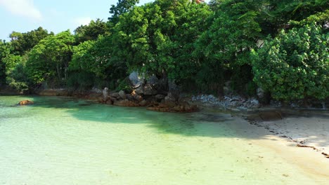 Hermosas-Piedras-En-La-Costa-De-Una-Isla-Tropical-Bajo-La-Sombra-De-Una-Exuberante-Vegetación-Bañada-Por-Aguas-Tranquilas-Y-Claras-De-La-Laguna-Turquesa,-Vietnam