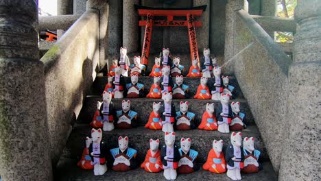Lento-Movimiento-De-Pedestal-De-Pequeñas-Estatuas-De-Zorros-En-El-Santuario-Fushimi-Inari-En-Japón-Durante-El-Día