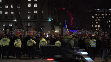 Antirassistische-Demonstranten-Mit-Antirassistischen-Plakaten-Und-Einer-Reihe-Von-Polizisten-Stehen-Nachts-In-Whitehall-Vor-Dem-Beleuchteten-London-Eye-Während-Einer-Protestaktion-Gegen-Premierminister-Boris-Johnson