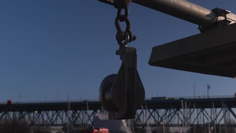 A-close-up-of-pulley-in-marina-bay-used-for-anchoring-boats-to-the-dock-lift-cargo-bridge-in-background-car-moving-across-blue-sky