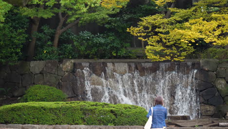 Slow-motion-of-a-woman-walking-towards-a-small-waterfall-in-Ueno-Park,-Tokyo