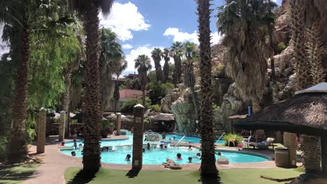 handheld-wide-shot-of-a-pool-lagoon-area-in-Avalon-Springs-Resort-Hotel-on-a-sunny-day-with-blue-sky-and-puffy-clouds