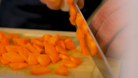 Chef-expertly-chopping-fresh-carrot-on-wooden-kitchen-board-with-steel-chief-knife,-handheld-close-up-shot