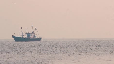 Un-Pequeño-Barco-De-Pescadores-Navegando-En-Medio-Del-Océano-Durante-La-Puesta-De-Sol-Con-Pequeñas-Olas-Tranquilas-Y-Regresando-A-Casa-En-Un-Fondo-De-Video-De-Clima-Brumoso-En-Mov-En-Full-Hd