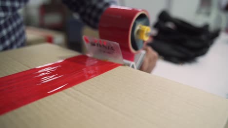 Factory-Worker-Taping-Cardboard-Box-For-Shipping-Logistics-In-Industrial-Workplace