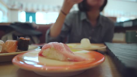 A-Serving-Of-Chutoro-Sushi-In-A-Plate---Woman-Eating-Sushi-In-A-Sushi-Restaurant-In-Numazu,-Japan---close-up,-selective-focus