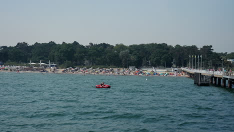 Weitwinkelaufnahme-Eines-Fahrenden-Tretbootes-Auf-Der-Ostsee-Mit-Timmendorfer-Strand-Im-Hintergrund