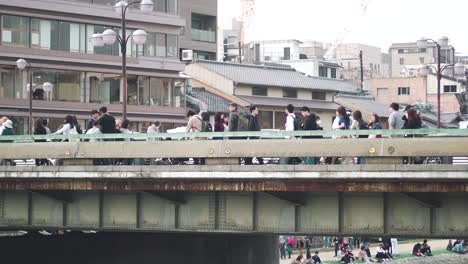Menschen,-Die-Tagsüber-Auf-Einer-Brücke-über-Den-Kamogawa-Fluss-In-Kyoto,-Japan,-Gehen-Und-Diese-überqueren