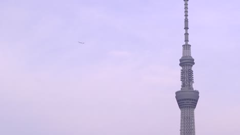 Nach-Oben-Geneigte-Aufnahme-Des-Tokyo-Skytree-Und-Eines-Fliegenden-Flugzeugs-Vor-Dem-Hintergrund-Eines-Blauen-Himmels