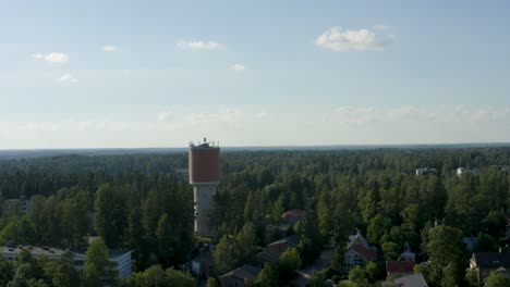 Aerial-reversing-shot-of-a-large-water-tower-above-the-trees-in-Finland