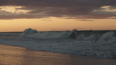 Große-Wellen-An-Einem-Strand-In-Neuseeland-Mit-Einem-Goldenen-Sonnenaufgang-Am-Himmel