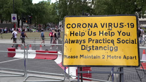 Menschen-überqueren-Einen-Fußgängerüberweg-Hinter-Einem-Gelben-Informationsschild-Mit-Der-Aufschrift-„Corona-Virus-19