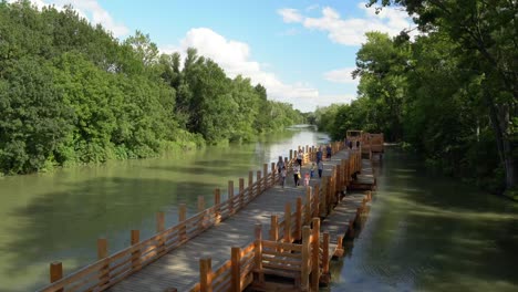 Families-walking-on-long-recreational-wooden-bridge-on-small-river