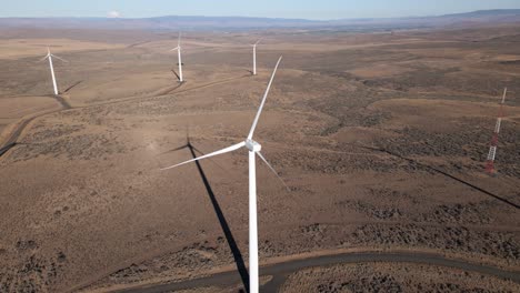 Long-shadows-stretch-across-the-desert-floor,-orbiting-a-giant-electric-wind-turbine,-aerial-panorama