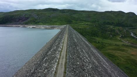 Drone-view-of-Norwegian-Dam-overlooking-lush-green-fields-and-mountains