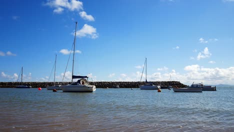 Luxurious-yachts-sail-boats-in-sunny-relaxing-shimmering-blue-sky-island-breakwater-ocean-coastline