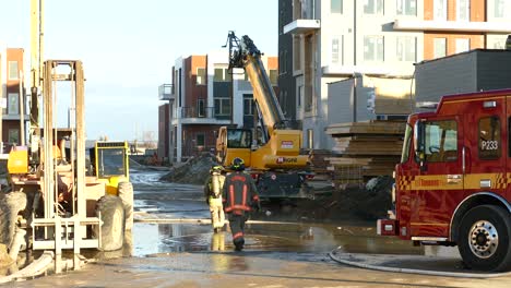 Wide-shot-of-two-exhausted-firefighters-walking-on-construction-site-after-blaze-during-sunny-morning