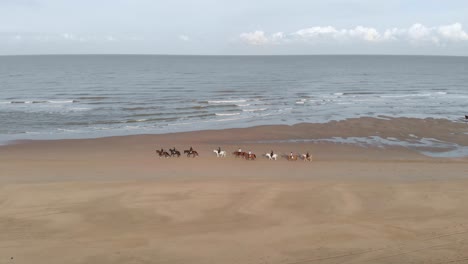 Luftaufnahme:-Reiter-Am-Strand,-Reiten-Auf-Sand-Mit-Meereswellen-Dahinter