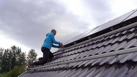 Technician-fastening-solar-panels-on-rooftop-during-installation-process---Static-with-male-worker-installing-panels-on-private-home-and-cloudy-sky-background