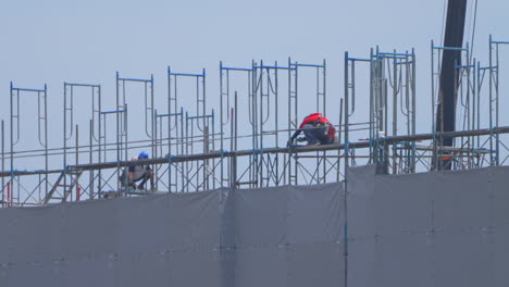 Dos-Trabajadores-De-La-Construcción-Japoneses-En-Equipo-Completo-Trabajando-En-La-Ola-De-Calor-En-La-Parte-Superior-De-Un-Edificio-Alto-En-Japón