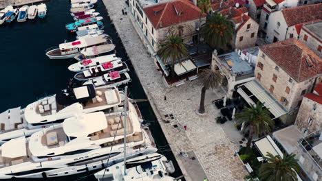 Super-Yachts-At-Marina-With-People-Walking-At-Promenade-Along-Waterfront-Buildings-In-Hvar,-Croatia