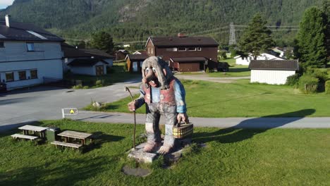 Norwegian-wooden-troll-statue-along-road-fv7-at-Flaa-Hallingdal---Rotating-around-troll-during-sunset---Houses-and-shops-in-background
