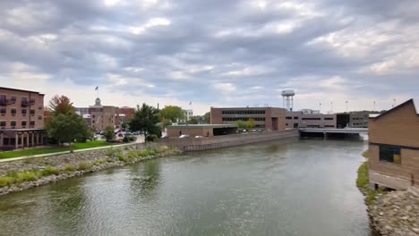 Drone-Flight-Over-Rock-River-Towards-Downtown-Buildings-In-Beloit,-Wisconsin-On-A-Cloudy-Day