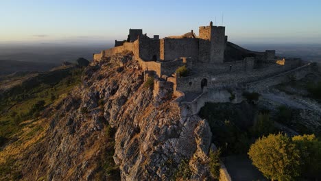 Eine-Drohne-Fliegt-Während-Eines-Goldenen-Sonnenuntergangs-An-Den-Mauern-Der-Burg-Marvao-Vorbei
