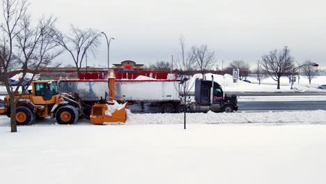 machine-clearing-a-pile-of-snow-on-the-streets-and-spewing-it-on-truck,-Canada-on-November-10,-2021