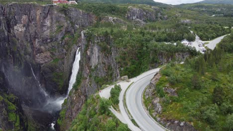 Tourist-standing-on-edge-of-cliff-to-watch-spectacular-waterfall-Voringsfossen-falling-of-Hardangervidda-mountain-plateu