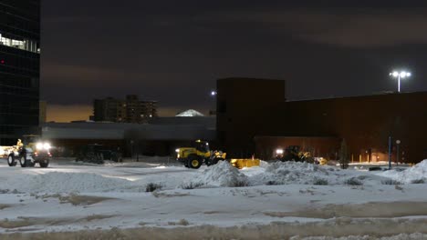 Tractor-cleaning-the-parking-lot-from-the-snow-during-a-snow-storm-at-blue-hour-in-Montréal,-Canada