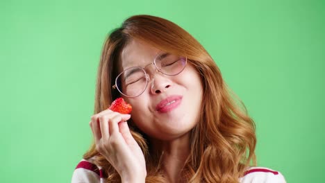 Young-woman-enjoying-strawberry-in-studio-with-green-screen-chroma-key-background