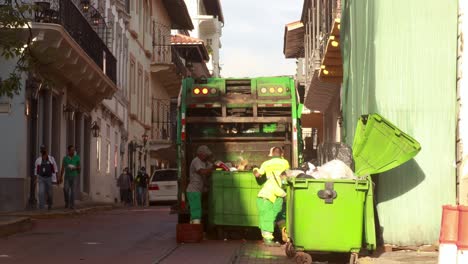 Empleados-De-La-Autoridad-Sanitaria-Trabajando-Arduamente-Vaciando-Los-Contenedores-De-Basura-De-La-Comunidad-En-La-Parte-Trasera-De-Su-Camión-De-Basura,-Casco-Viejo,-Ciudad-De-Panamá