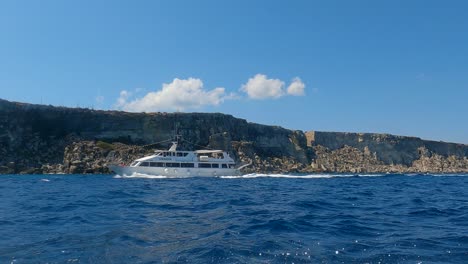 Low-angle-sea-level-view-from-sailing-boat-of-touristic-boat-crossing-scene-at-Favignana-island-coast-in-Sicily,-Italy