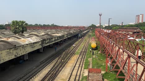 Pan-view-from-left-to-right-of-a-railway-station-and-an-over-bridge-for-people-to-cross-the-railway-tracks-in-Kamalapur,-Bangladesh