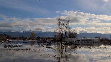 Die-Spiegelglatte-Oberfläche-Einer-überschwemmten-Farm-Und-Eines-Gewächshauses-In-Abbotsford-Spiegelt-Einen-Blauen-Himmel-Und-Einige-Leichte-Wolken-Wider