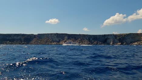 Low-angle-sea-level-view-from-sailing-boat-oftouristic-boat-navigating-along-Favignana-island-coast-in-Sicily,-Italy