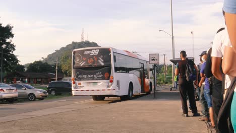 Bus-arriving-at-the-bus-stop-to-a-line-of-commuters-waiting-patiently-outside-Albrook-Metro-station,-everyone-wearing-protective-facemasks-and-practicing-social-distancing