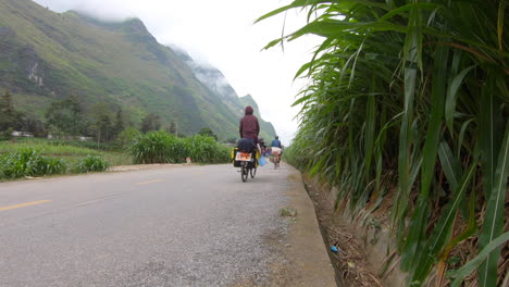 Travelers-on-bicycles-riding-along-the-side-of-a-road-while-motorcycles-pass-in-a-valley