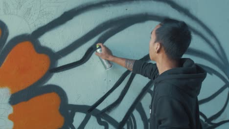 Young-male-graffiti-artist-spraying-design-on-wall