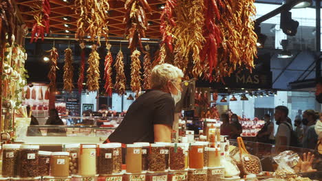 Barcelona---Mercado-de-La-Boqueria,-stall-selling-dried-spices-and-herbs-with-vendor-wearing-a-mask